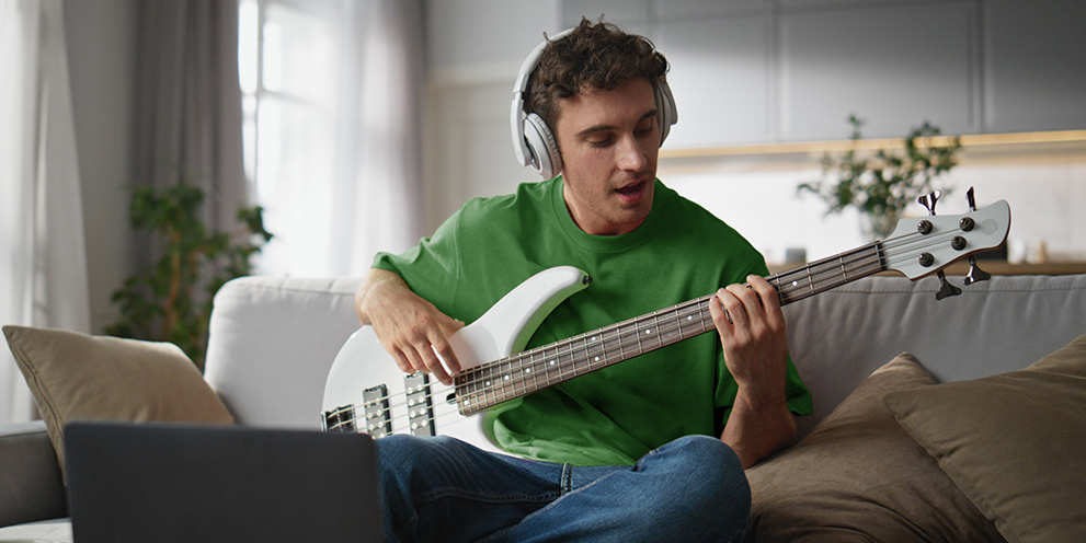 Man wearing headphones playing bass guitar at home