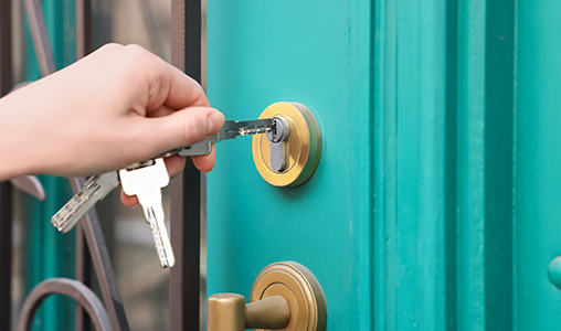Hand unlocking a turquoise front door with keys