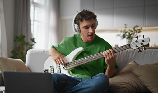 Man wearing headphones playing bass guitar at home