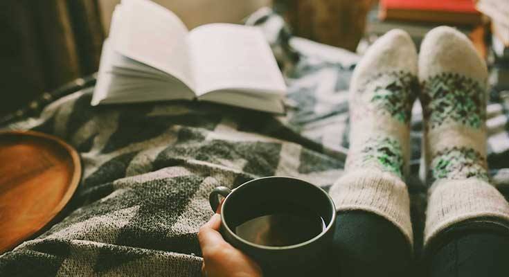 Person relaxing at home with hot drink and book.