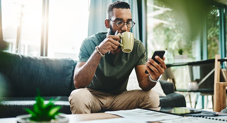 A man drinking a coffee whilst looking at their mobile.